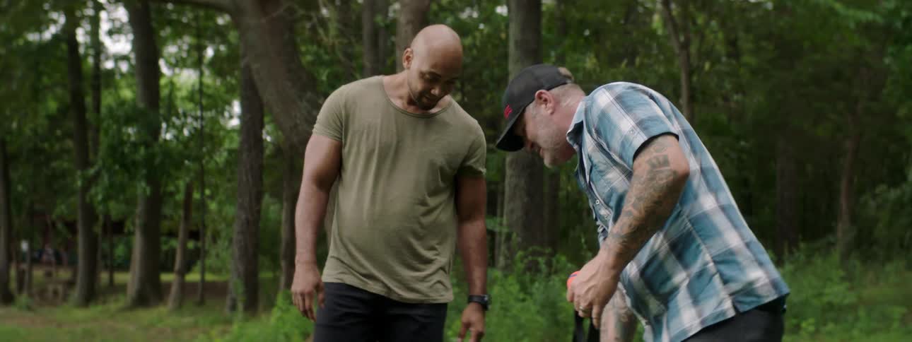 Two men shake hands outside while one of them holds the leash to his dog
