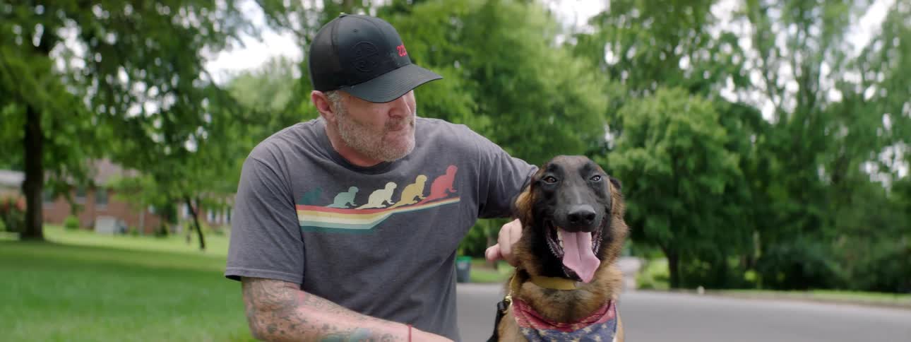 A man with a hat kneeling down and stroking a dog
