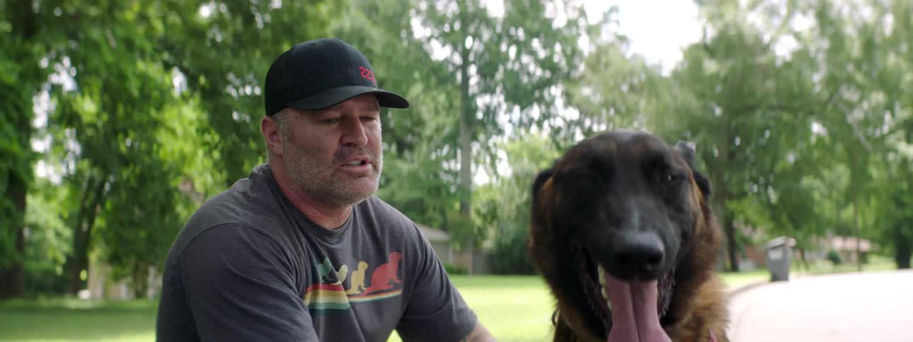 A man sits outside near a neighborhood road petting his dog