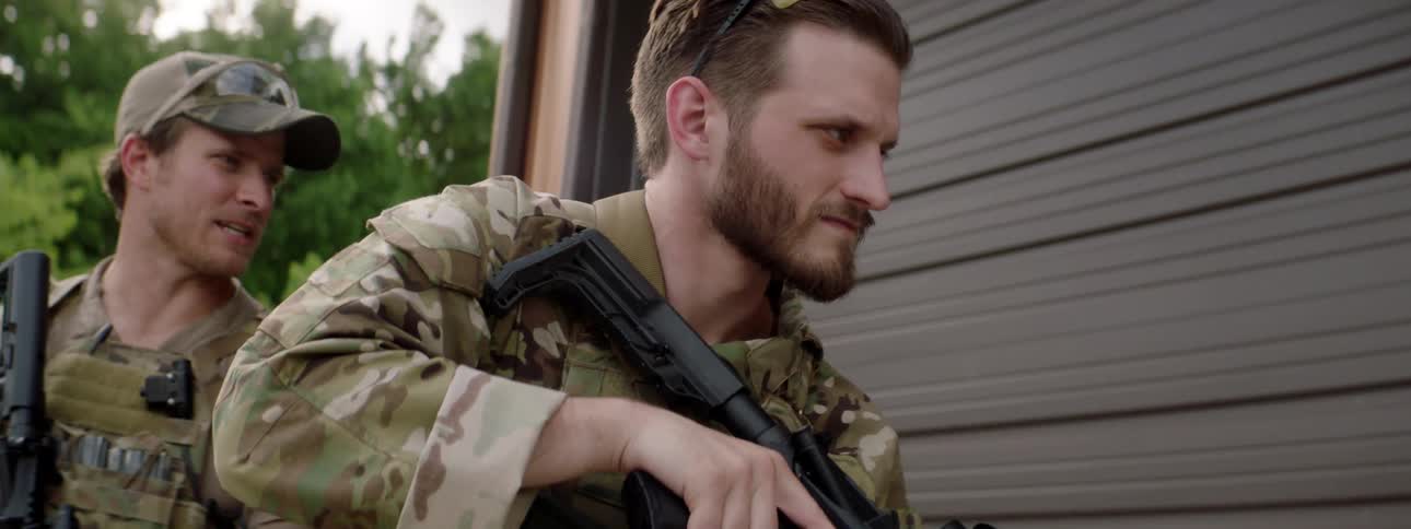 Two soldiers stand outside a building with their guns drawn