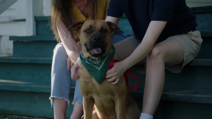 Two people pet their dog on the porch