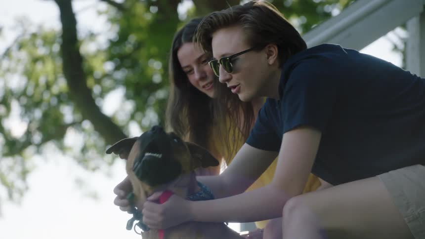 A boy and a girl playing with a dog with trees and the sky in the background