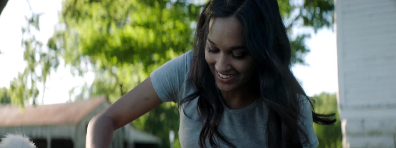 A smiling woman sits outside playing with a pet dog