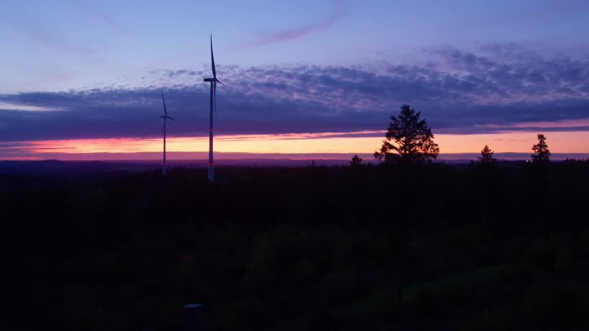 The sun is setting behind the windmills