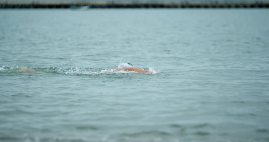 Muscular man with goggles and a swim cap swims through sea water