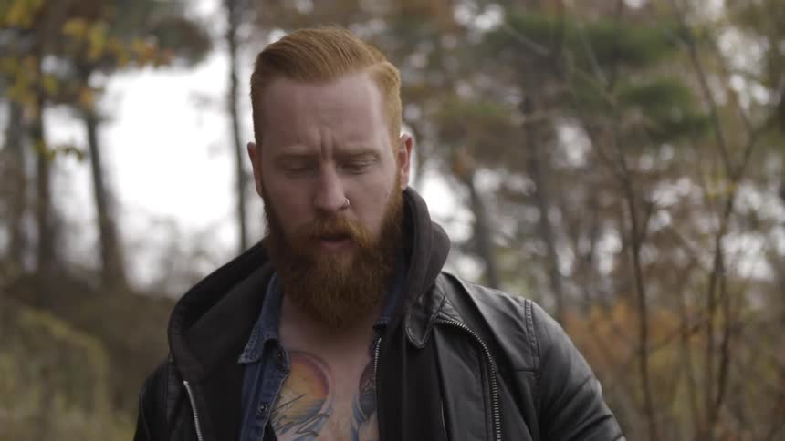 Bearded man with a tattooed chest walking through the woods