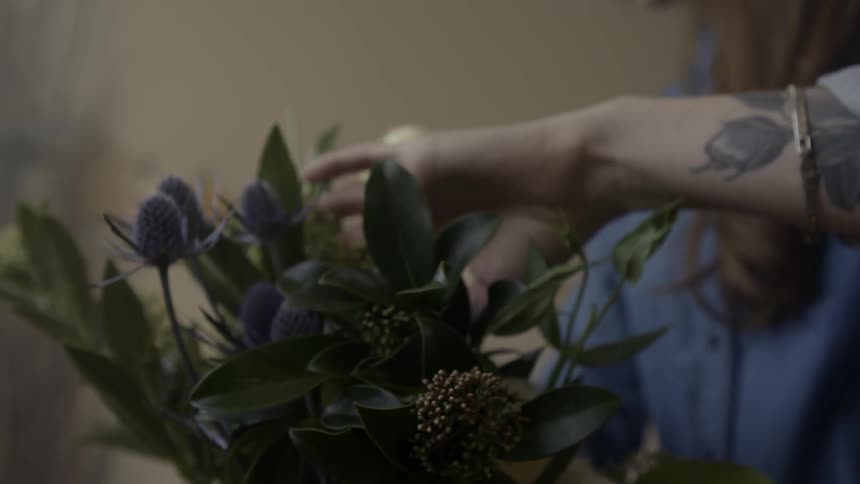 A woman is placing flowers into a bouquet