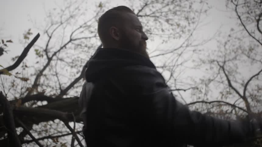 A man standing next to a fallen tree whips an object into the distance
