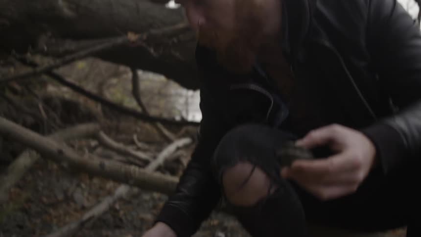 A man is foraging around on the ground near a tree