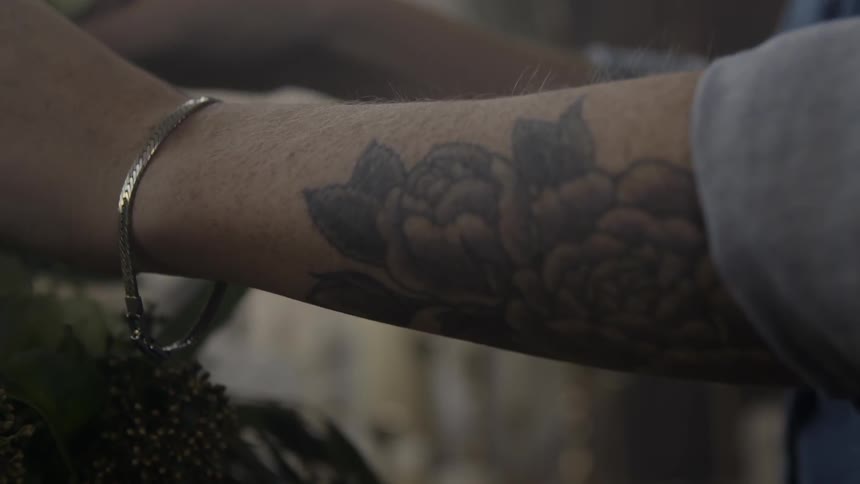 Tight shot of a tattoo on a woman's forearm as she arranges flowers