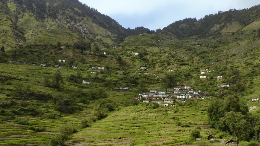 A remote village is located on a green hillside that leads up to a range of mountains