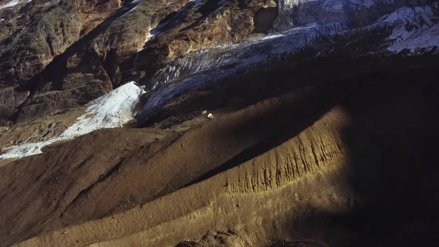 Mountain slope partly covered in shadows is dusted with snow
