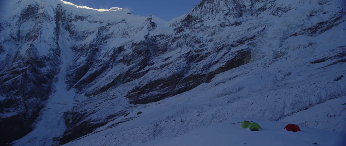 Three tents in the tundra with a snow covered mountain and the sky in the background