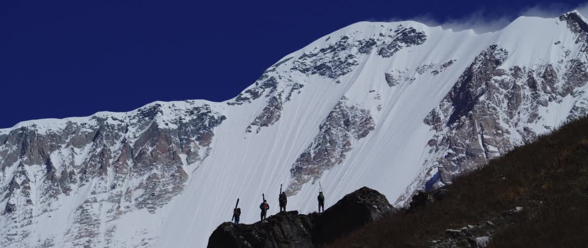 Four people standing on a cliff with a mountain range with snow and ice in the background
