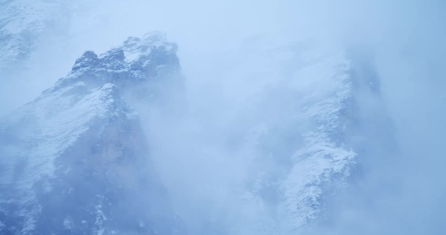 A snowy mountain ridge shrouded in thick fog during the day