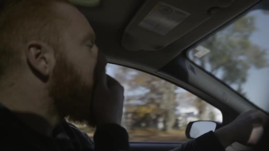 A man rubs his face while driving