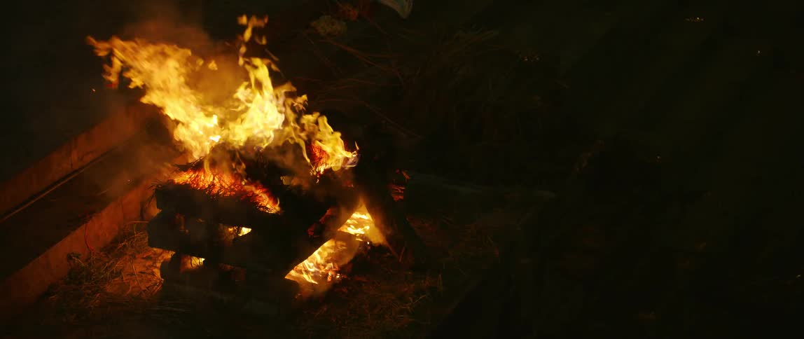 A campfire made with thick pieces of wood burns tall and bright at night