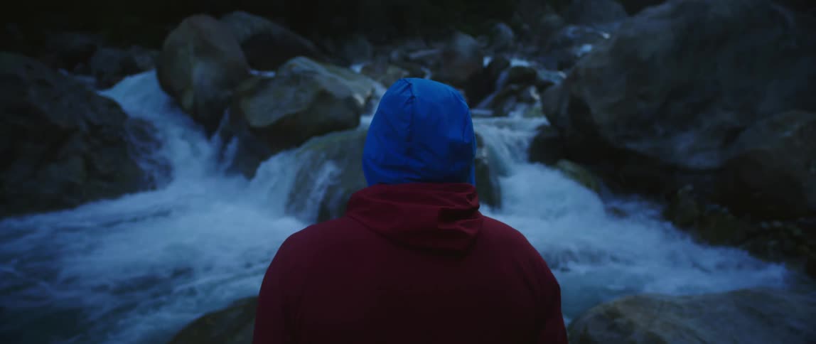 A person stands on a boulder in the middle of a river in the evening