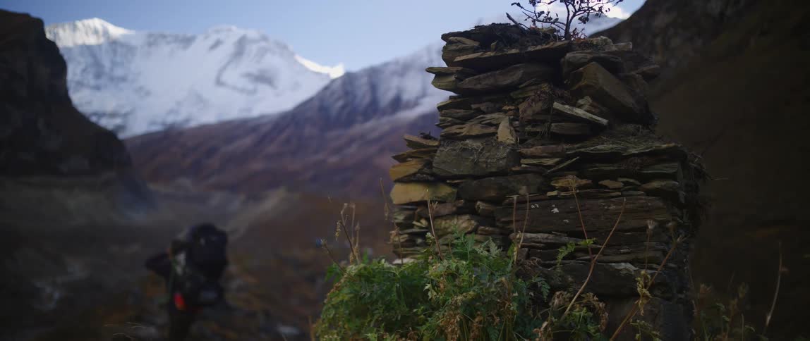 Hiker walks along trail toward snow covered mountain away from stacked wooden