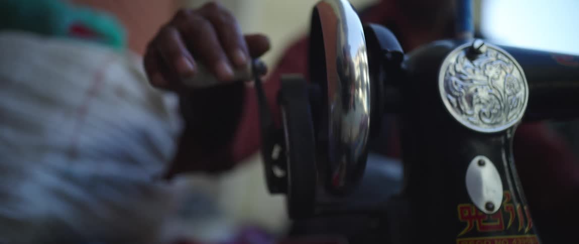 A person in a room with a window in the background turning a lever on a sewing machine