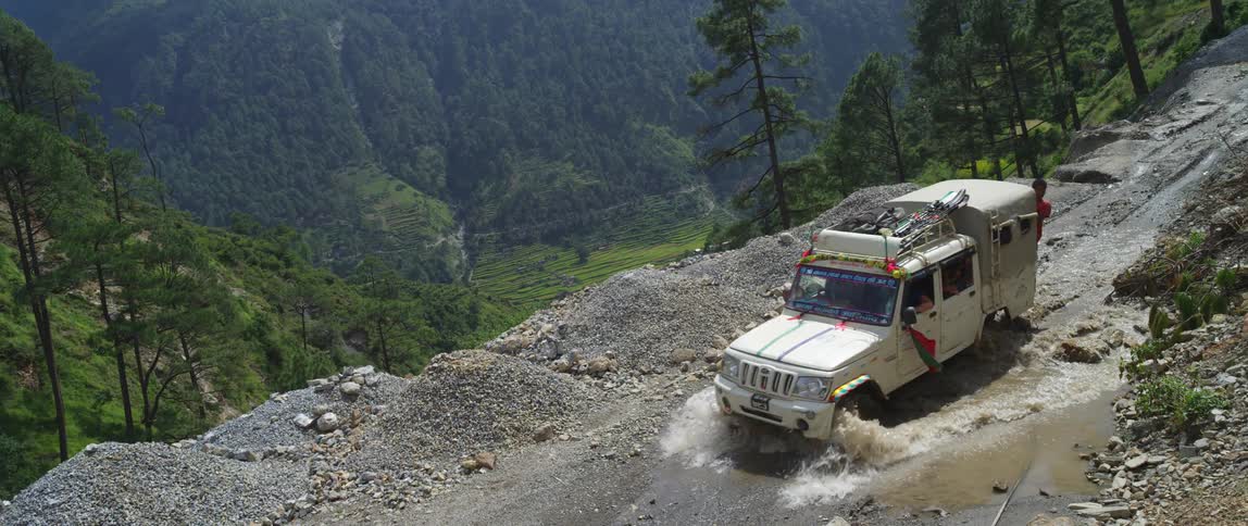 A vehicle with people driving on a dirt road over a puddle on a cliff