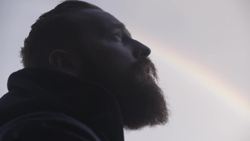 A man is looking around with a rainbow behind him