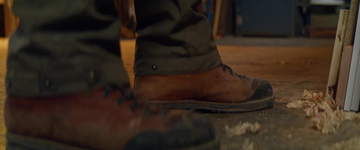 The feet of a man as he shaves a piece of wood in a workshop