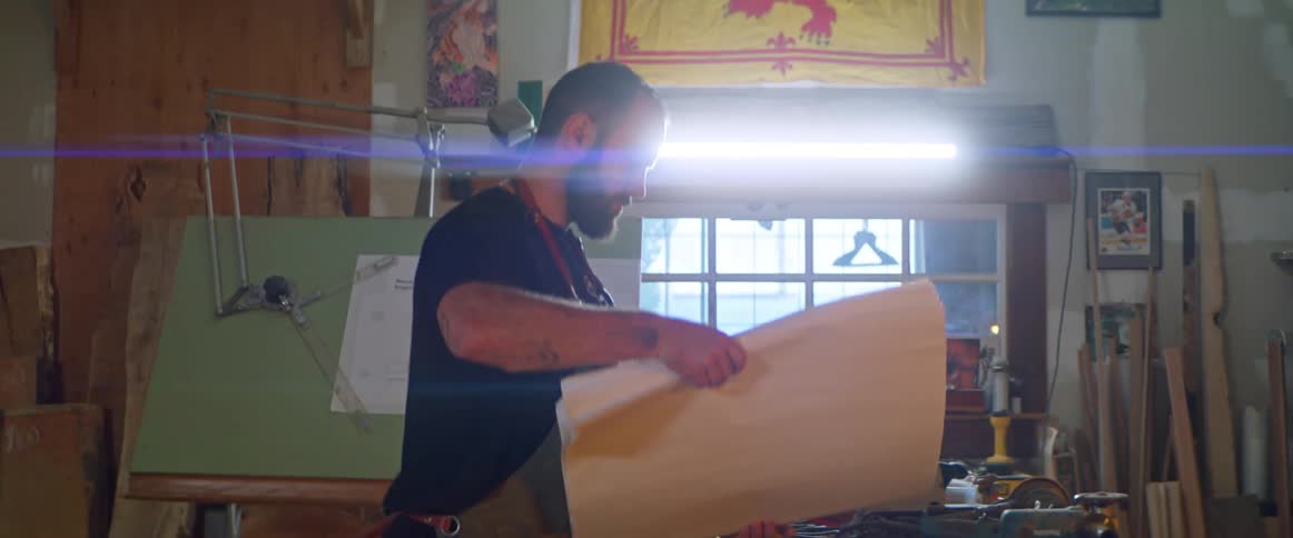 A man opens up blueprints on a table in a workshop