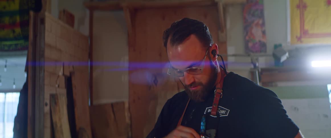 A man in a workshop puts in ear plugs and adjusts the tools on his apron