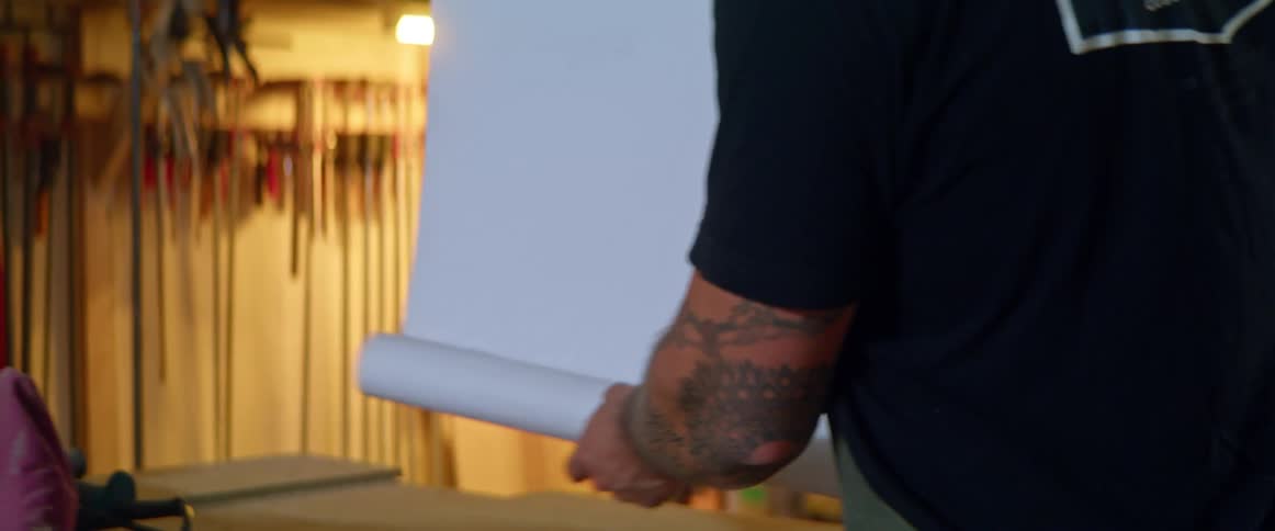 Man unrolls and rolls drafting paper on table in workshop