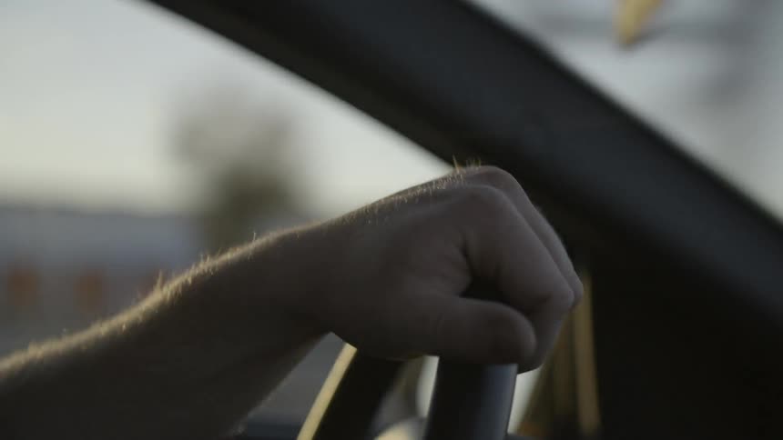 The sun shines on a man's arm as he drives a car