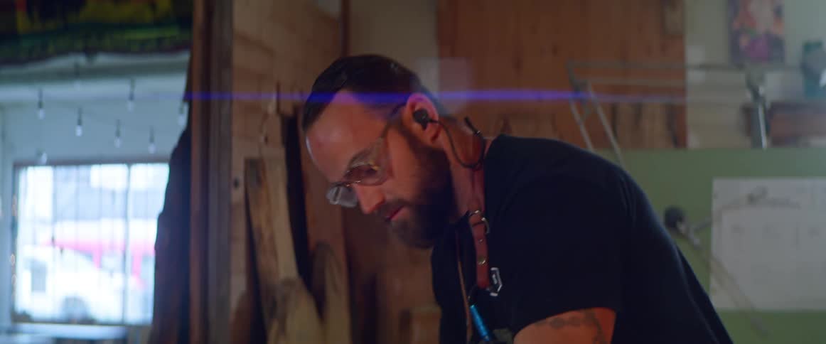 A man works in a workshop as cars drive by outside