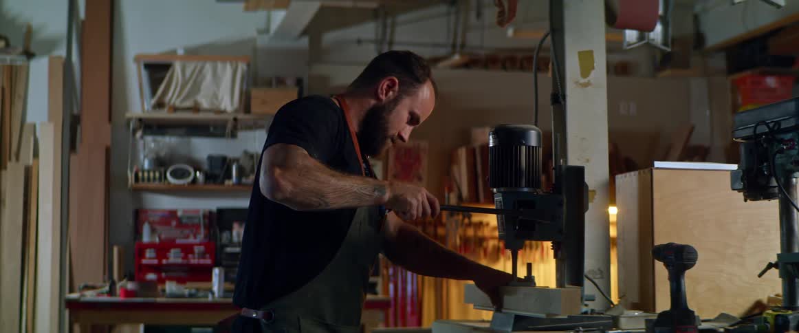 A man pushes the level on a drill press standing in a large garage
