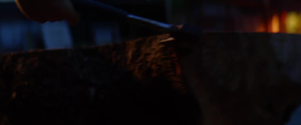 A person drives a hatchet into a split log outside of a building in the evening