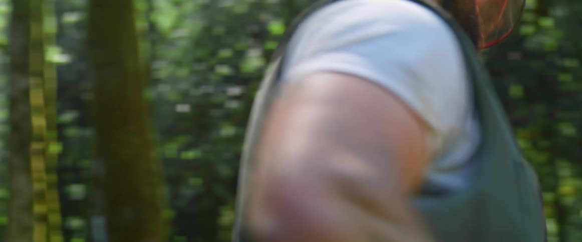 Man with helmet carries a big chainsaw in the woods