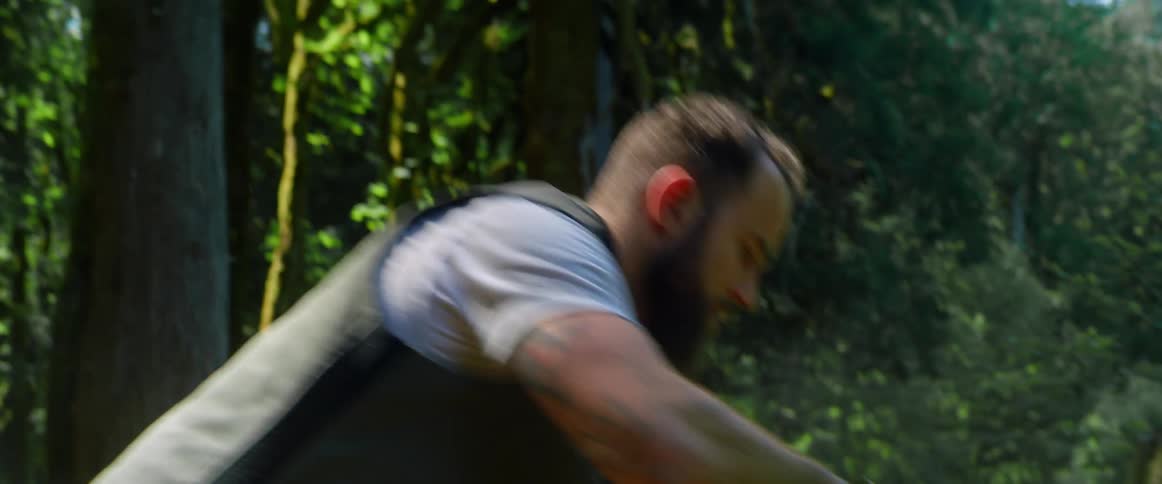 A man uses a strap to wrap around a large tree log in a woodland area