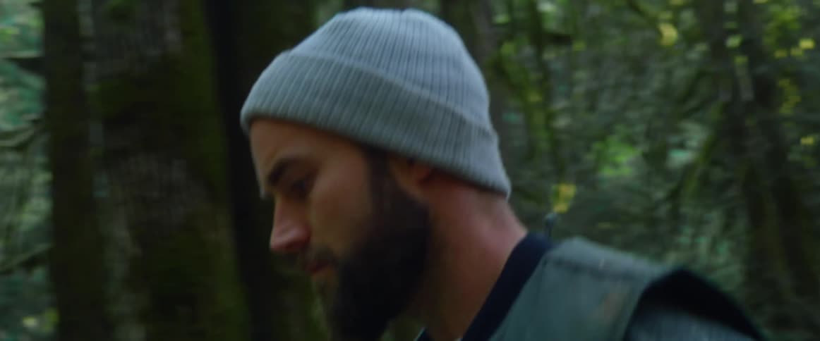 Man carrying chainsaw walks through pine forest in daytime