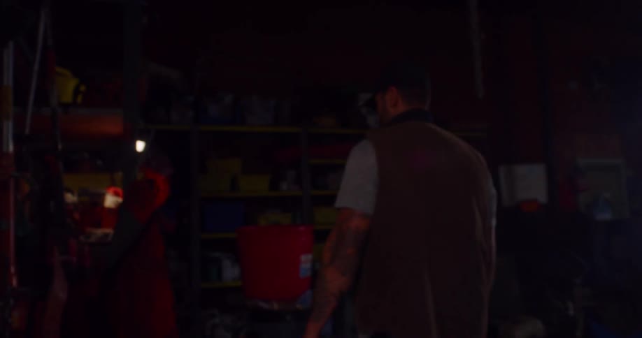 A man opens a door to a large rural shed and walks inside to retrieve a tool