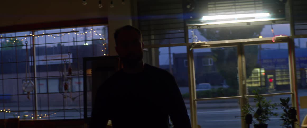 A man walks through the front of a store while carrying a coffee mug in the evening