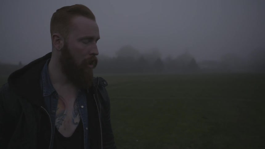 A man is smoking a cigarette on a field on a foggy day