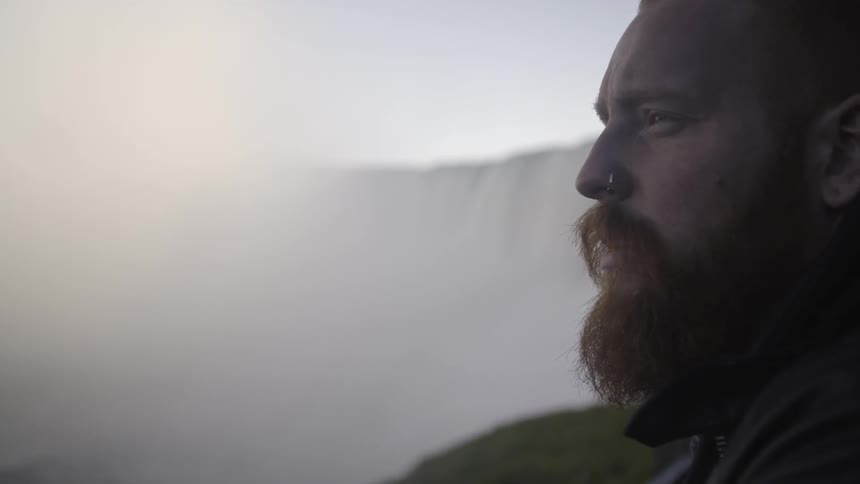 A bearded man looks out over a waterfall
