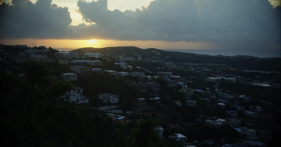 Sun rises from horizon toward clouds over mountains bordering town