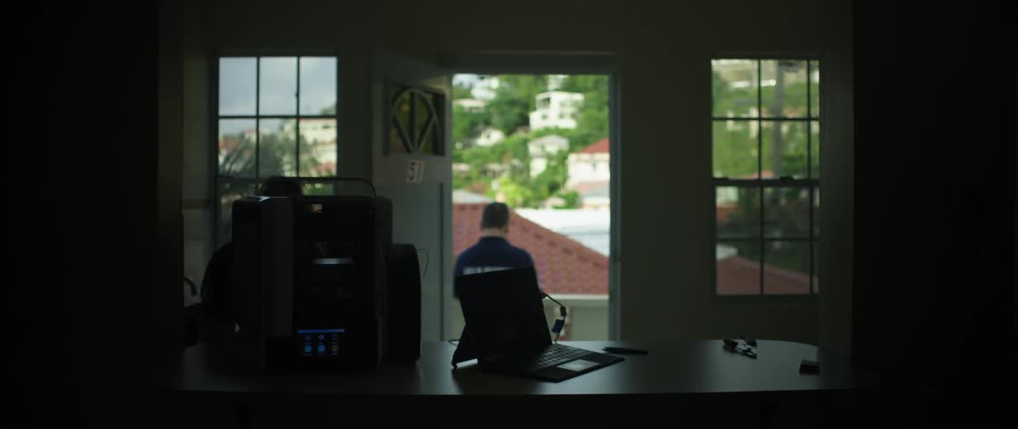 A person standing on a balcony at home while another is inside
