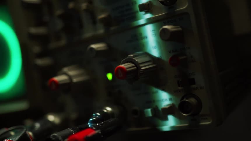 Close up of the dials and knobs of an oscilloscope in a dimly lit room