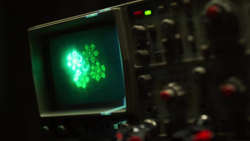 Light flows across front of oscilloscope with bright green shapes displayed on monitor