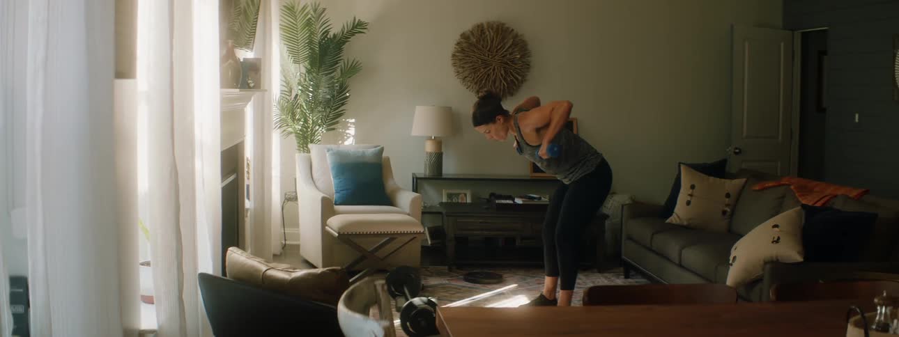A woman lifts dumbbells in the living room of a house during the day