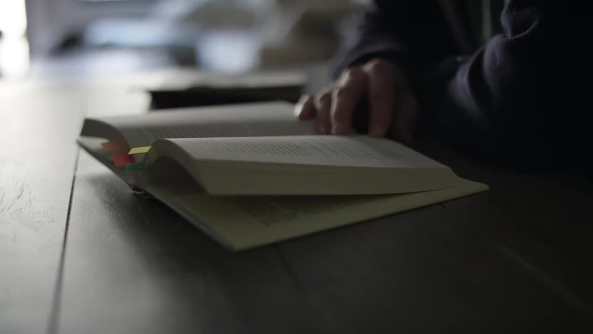 Man with a beard and and glasses sitting at table reads a book