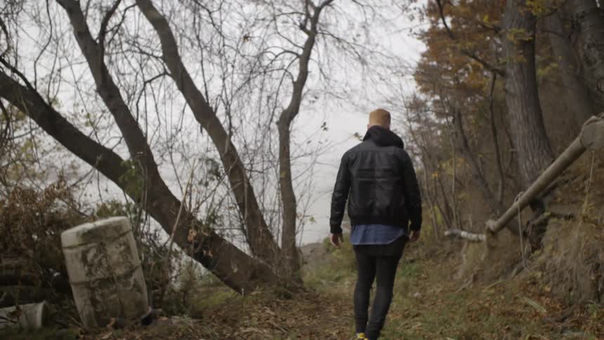 A man in a black jacket walks between trees