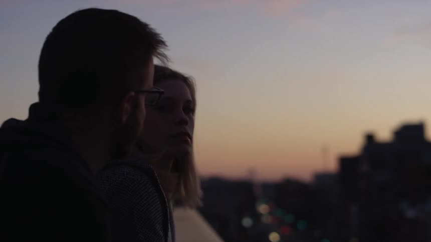 Woman joins man hugging his arm as they look out on city at night