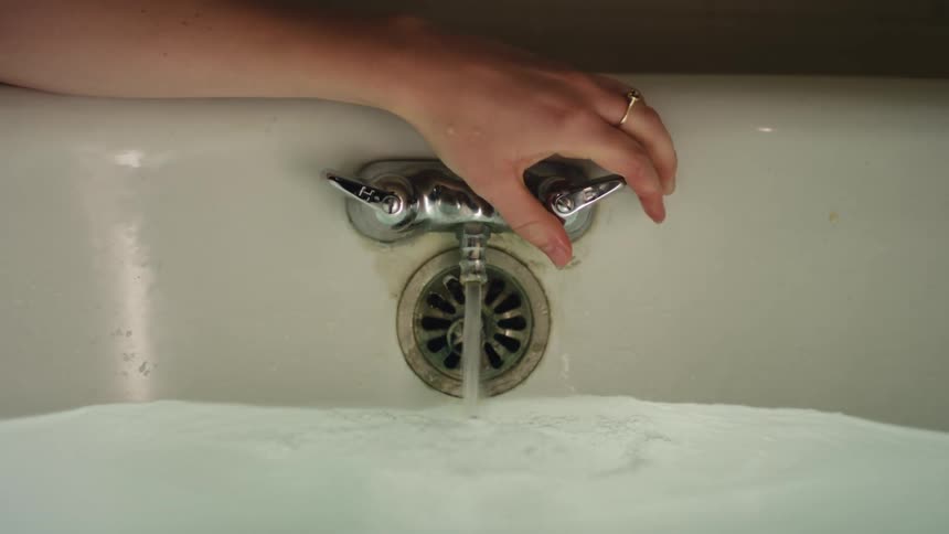 A person turns the water on in the tub